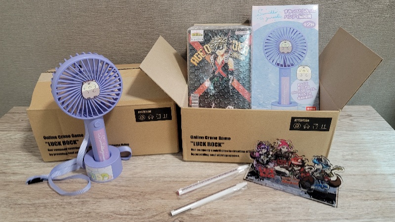 LUCK ROCKから実際に自宅へ届いた景品の写真。LUCK ROCKのロゴが入った段ボール箱とポータブル扇風機、漫画本などの景品